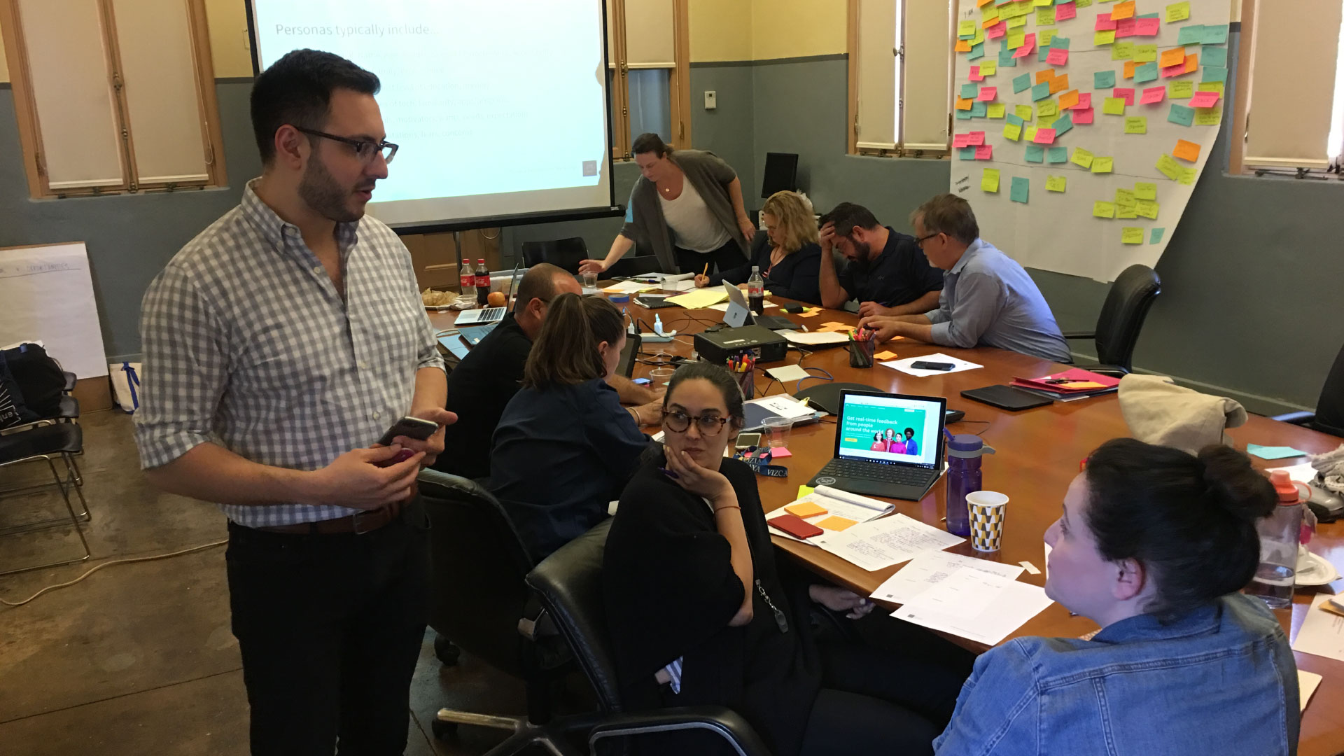 Michael Tedeschi facilitating a design thinking workshop with participants around a table with sticky notes in the background. 